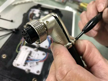 Technician soldering wires to a right-angle GX16 connector during cable assembly Technician soldering wires to a right-angle GX16 connector during cable assembly